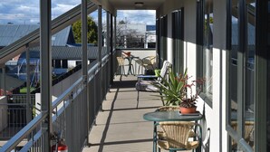 A balcony with a view of neighboring buildings, a small table with chairs, and a potted plant. - Darfield Motel (Darfield)