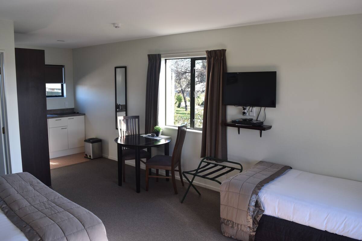 Una habitación de hotel con una cama, un escritorio con silla, un televisor y una ventana con cortinas.