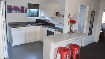 Una cocina moderna con armarios blancos, microondas, fregadero y una pequeña isla con dos taburetes rojos.