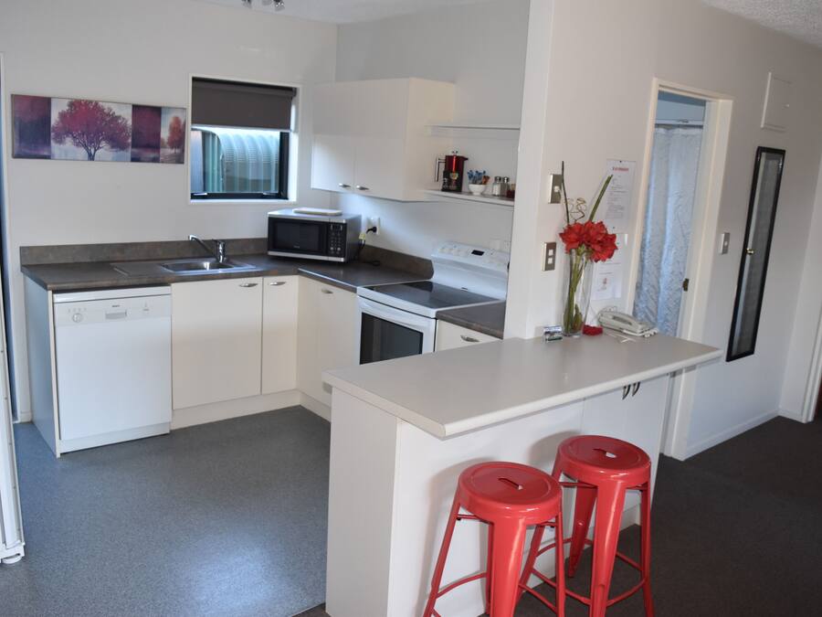 Una cocina moderna con armarios blancos, microondas, fregadero y una pequeña isla con dos taburetes rojos.