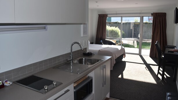 A modern kitchen with a built-in oven, a sink, and a countertop. There is a bed with a view of the outdoors. - Darfield Motel (Darfield)