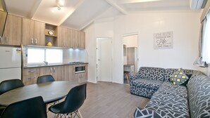 A modern living space with a kitchen, dining area, and a patterned sofa. - Warragul Gardens Holiday Park (Warragul)