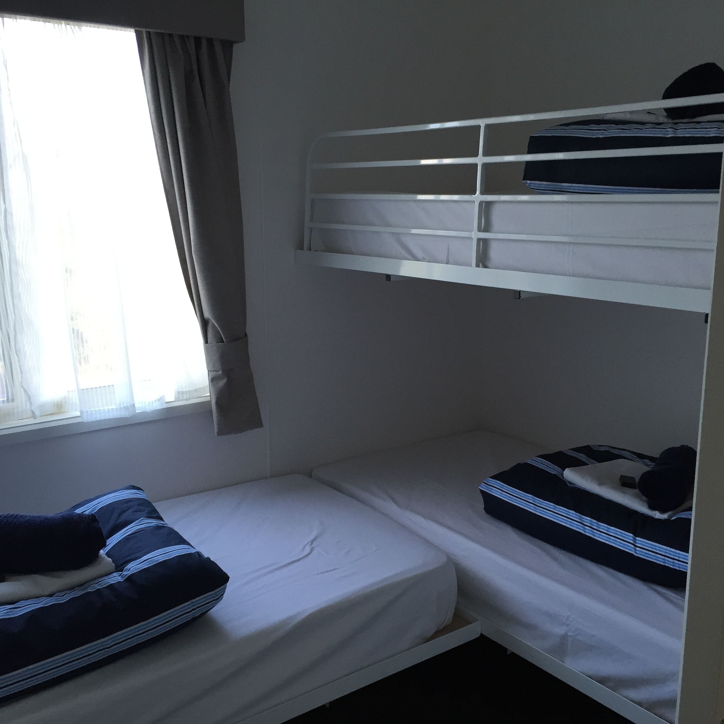 Una camera con un letto a castello, una finestra, tende e un letto con un cuscino.