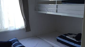 Una camera con un letto a castello, una finestra, tende e un letto con un cuscino.