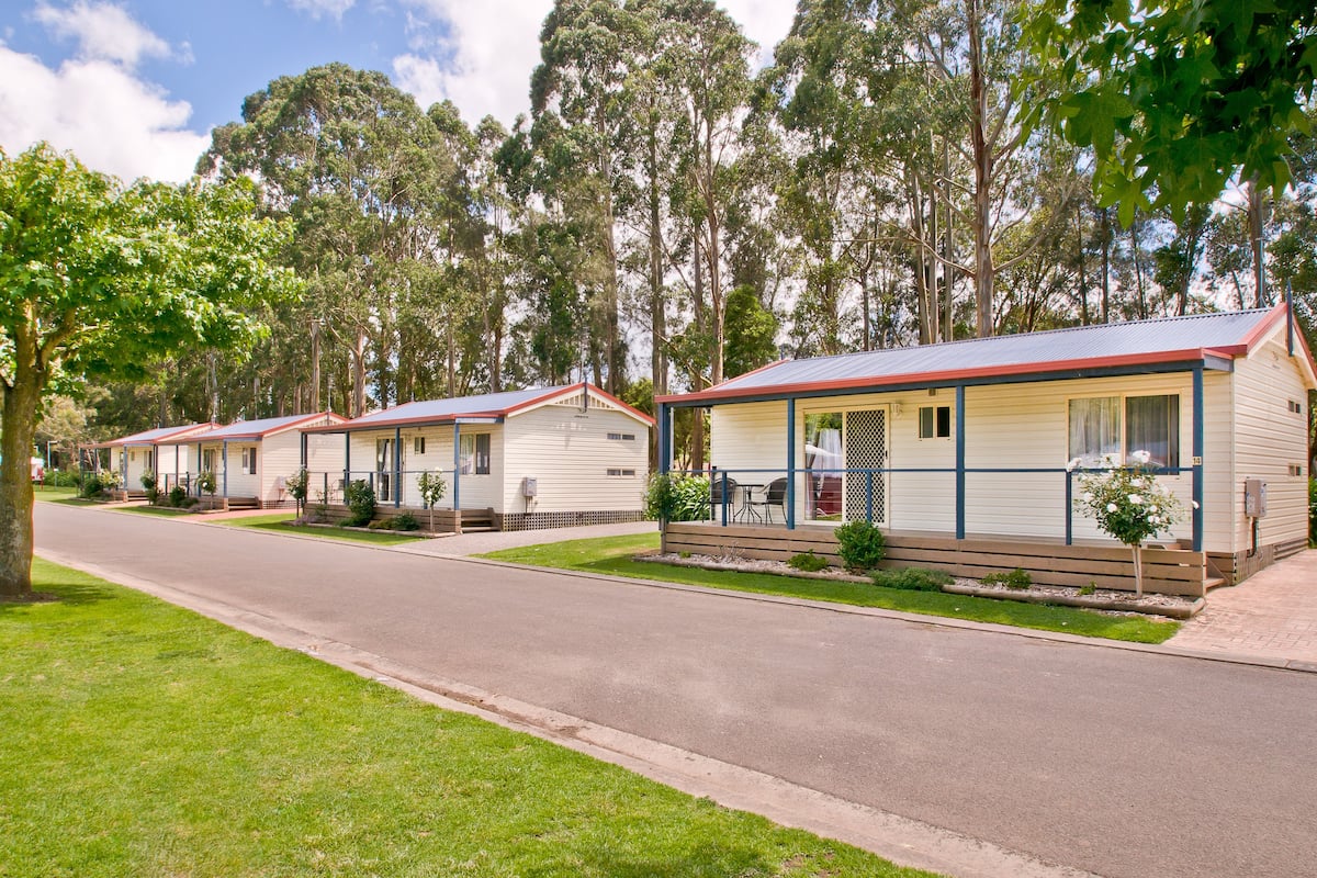 A row of mobile homes with a paved driveway and a grassy area in front.