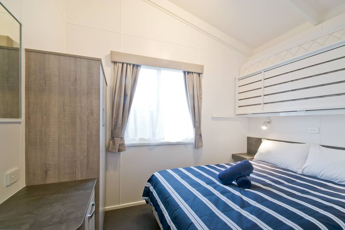 A bedroom with a bed, a nightstand, a window with curtains, and a wardrobe.