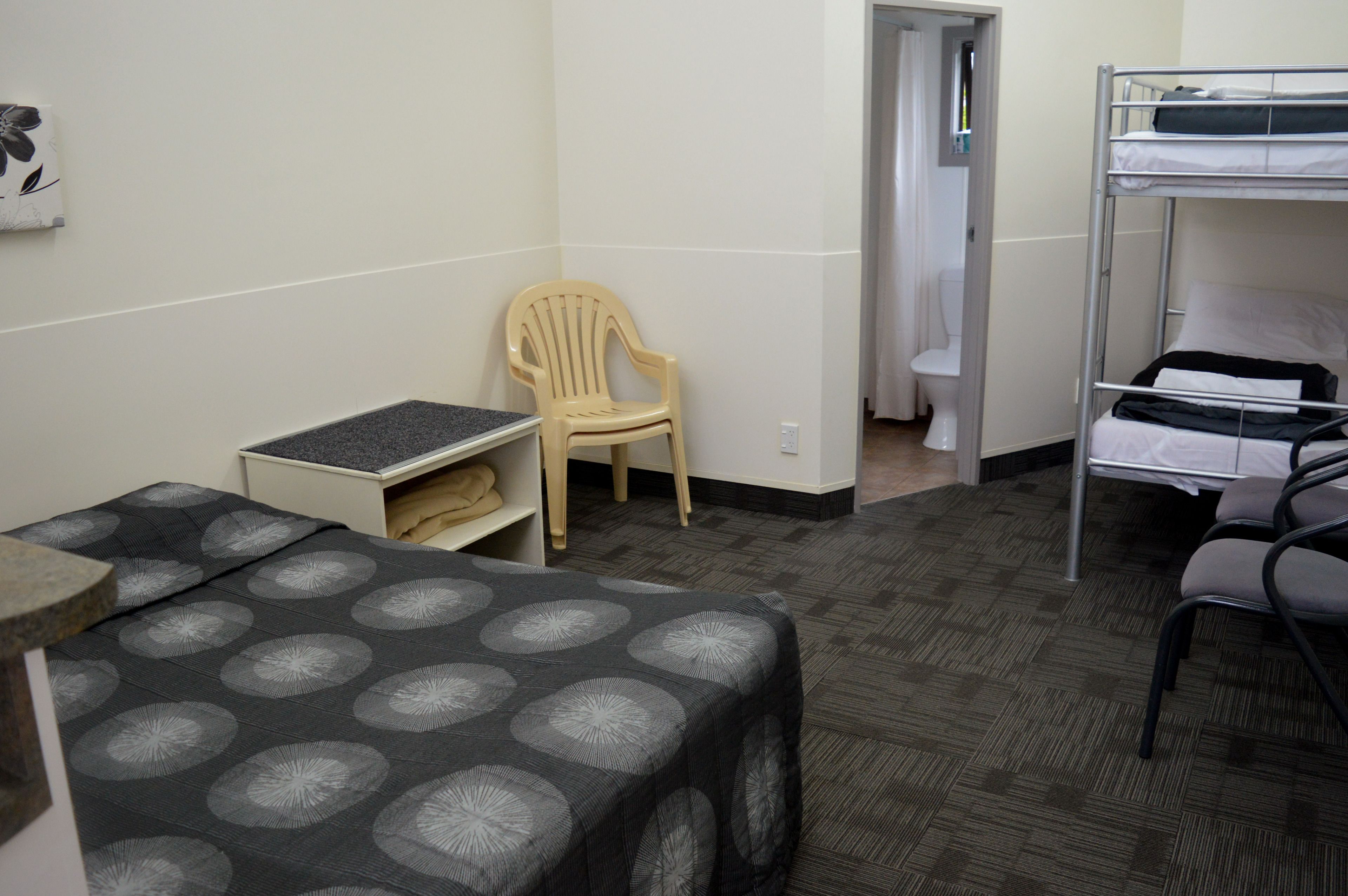 A small, compact room with a bunk bed, a single chair, a small table, and a desk.