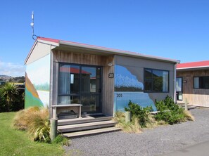 A small building with a number 205, a bench outside, and a mountain painting on the side. - Dunedin Holiday Park & Motels (Dunedin)