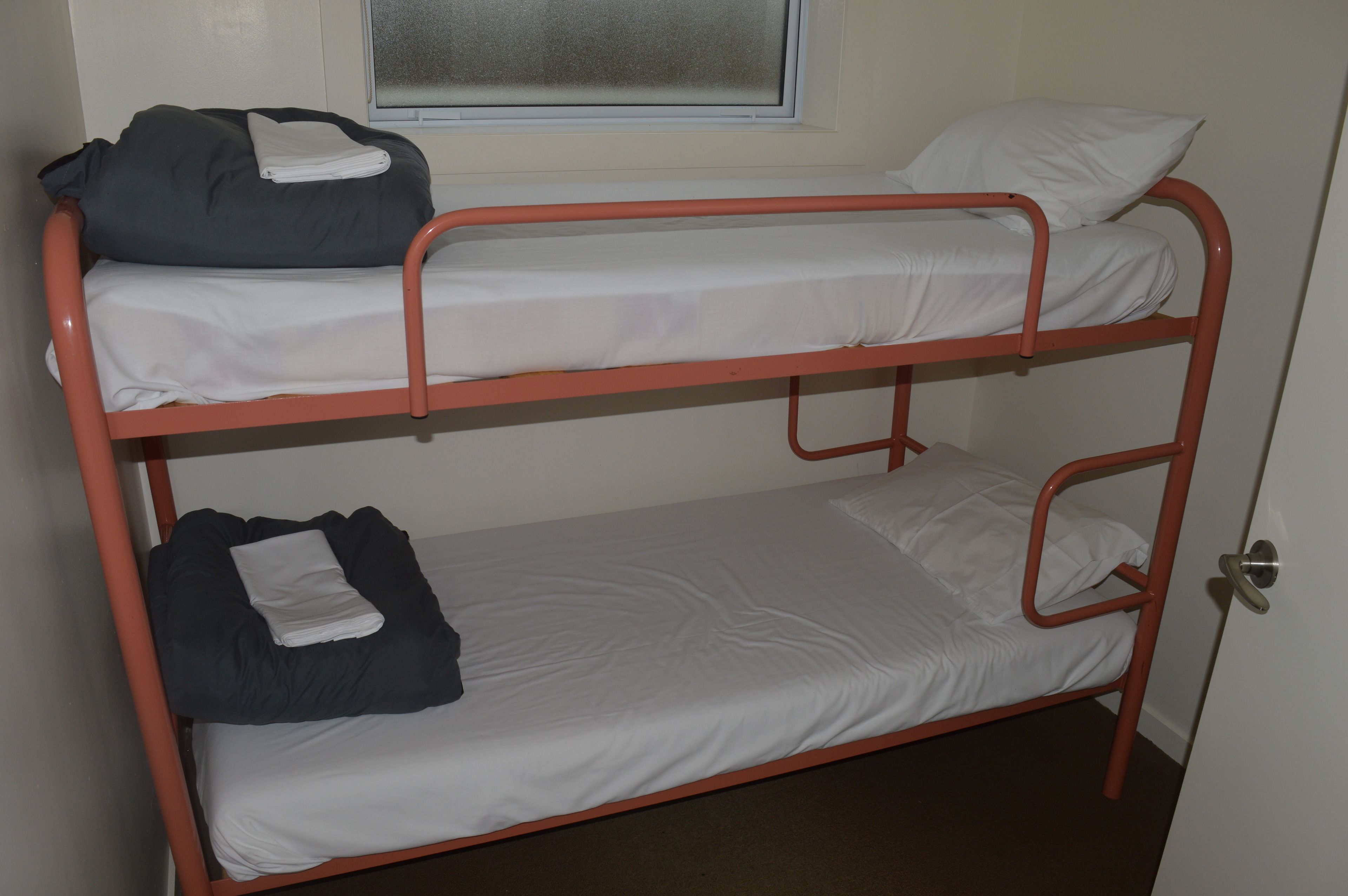 Un letto a castello con due letti, una finestra sopra e una porta alla destra.