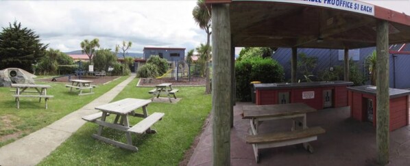 A covered picnic area with picnic tables and a small building with a sign.