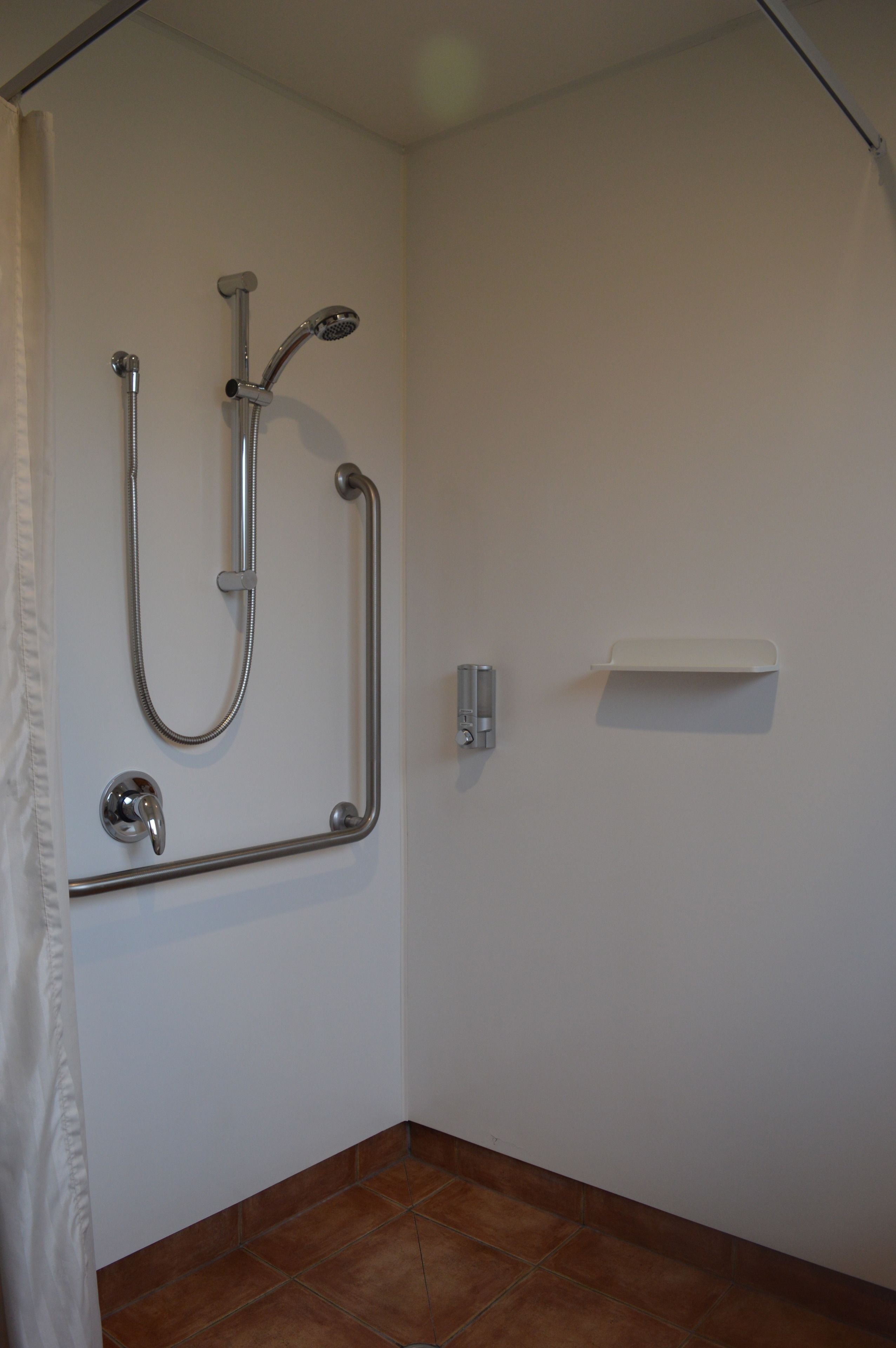 A bathroom with a shower, grab bar, and a small shelf.