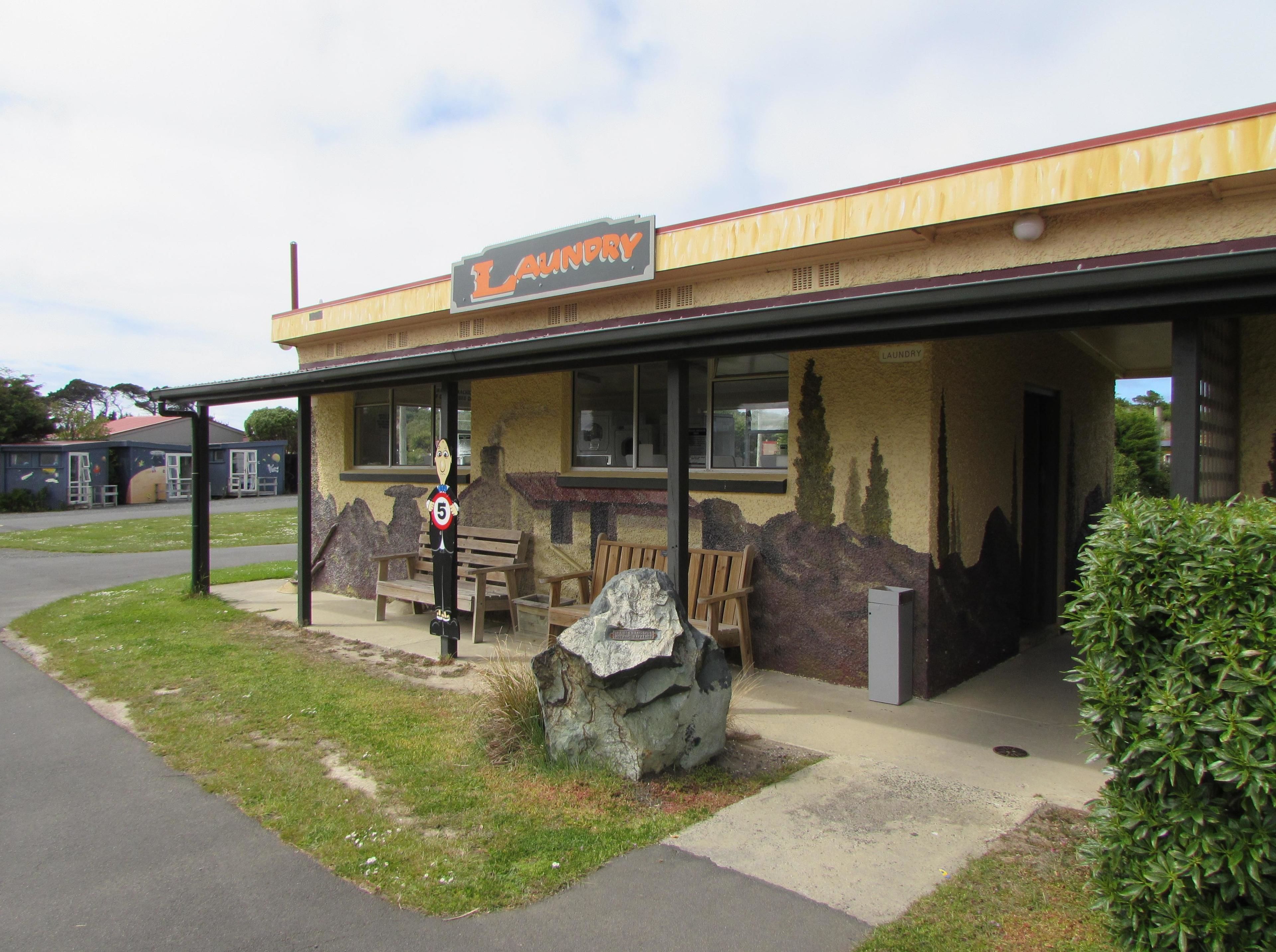 A laundromat with a sign, outdoor seating, and a large rock in front.