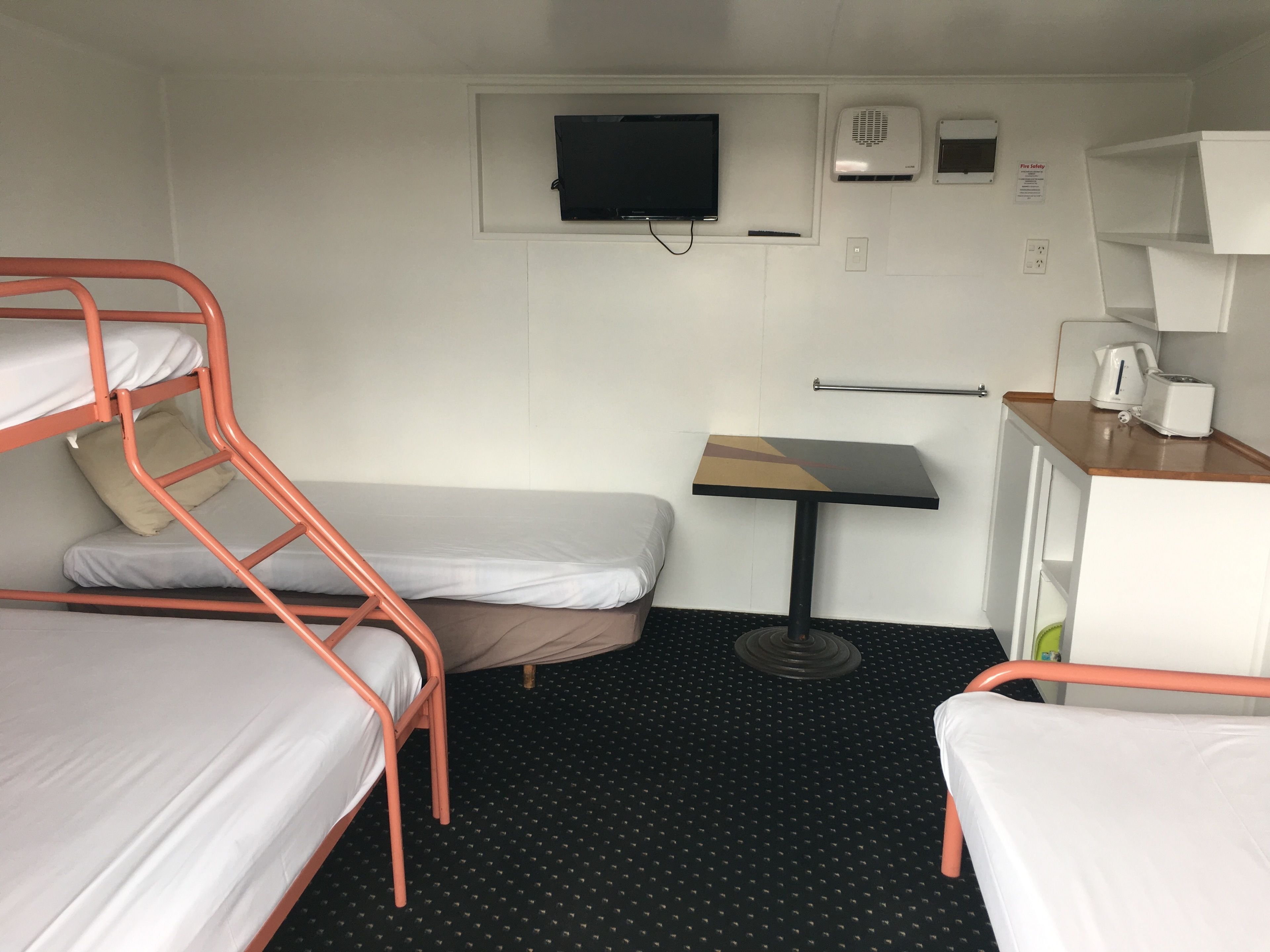 A compact room with bunk beds, a small table, a television, and a kitchenette.
