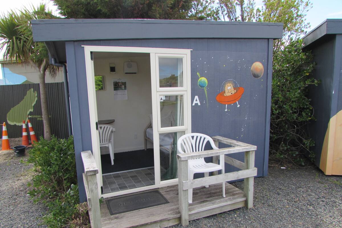 A small, single-room structure with a door, a window, and a bench outside.