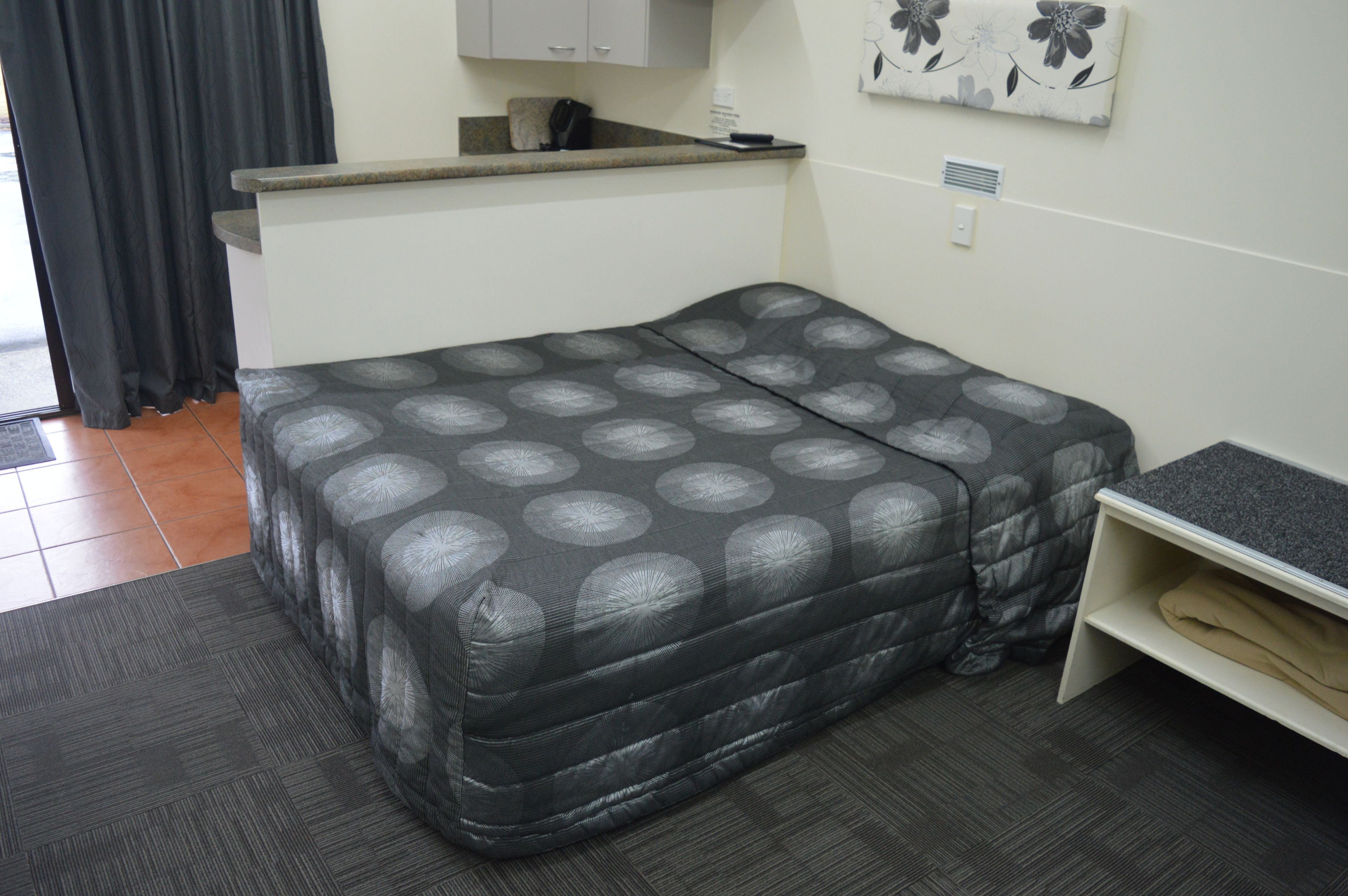 A compact room with a bed, a small desk, and a kitchenette area.