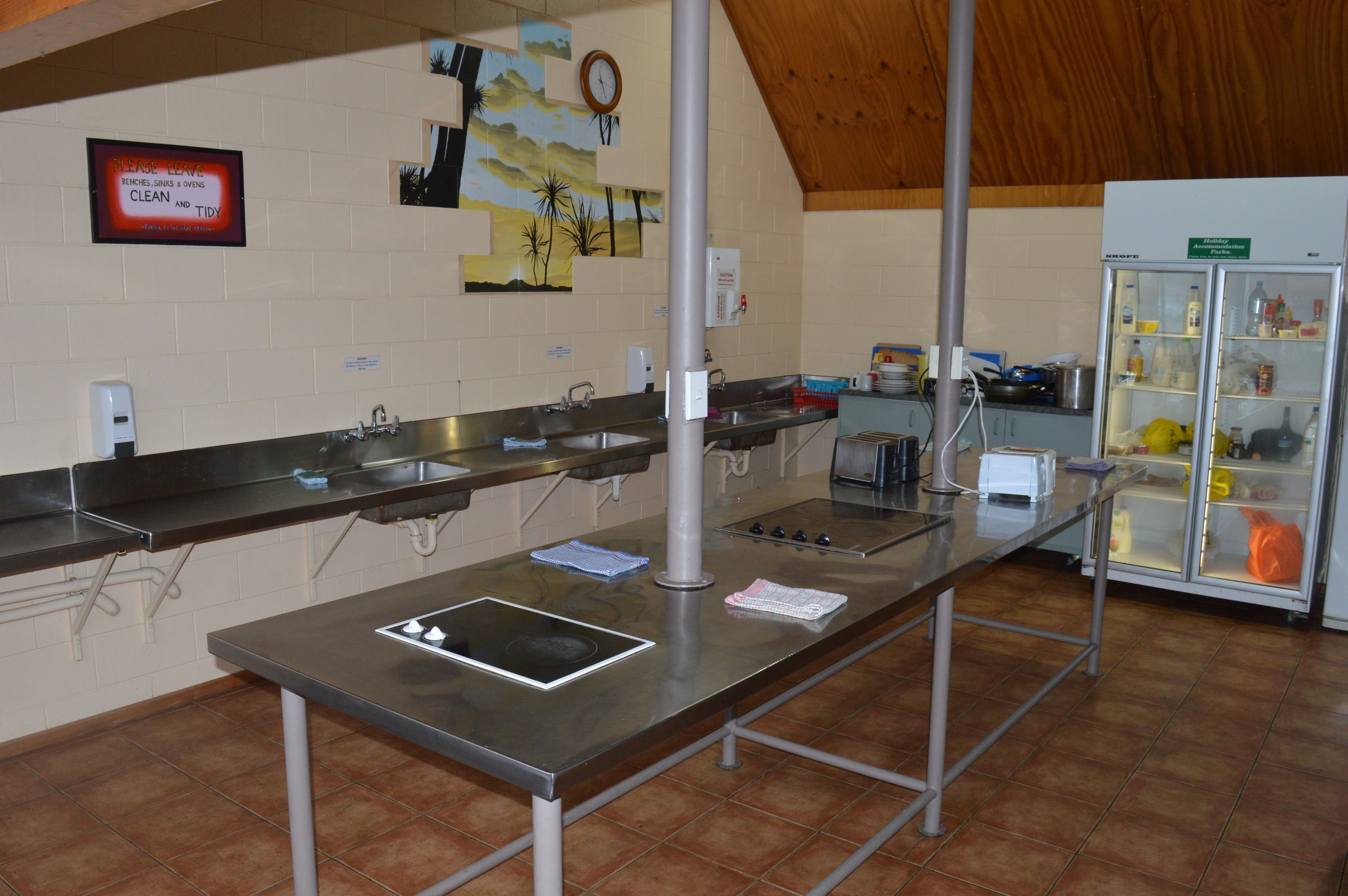 A kitchen with stainless steel countertops, a refrigerator, and a clock on the wall.