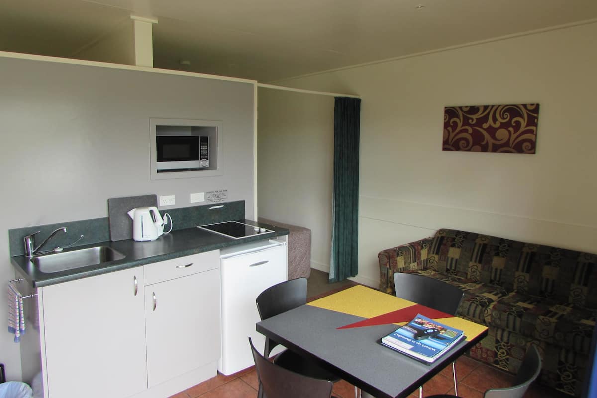 A compact kitchenette with a microwave, sink, and small refrigerator. There is a dining area with a table and chairs, and a patterned sofa.