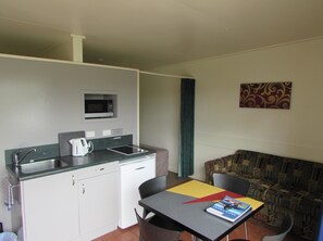 A compact kitchenette with a microwave, sink, and small refrigerator. There is a dining area with a table and chairs, and a patterned sofa.