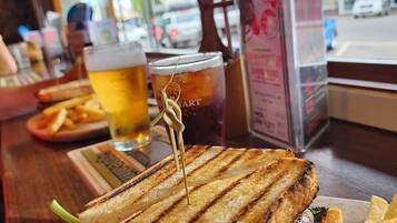 En smörgås med en tandpetare i, ett glas öl och pommes frites på ett bord.