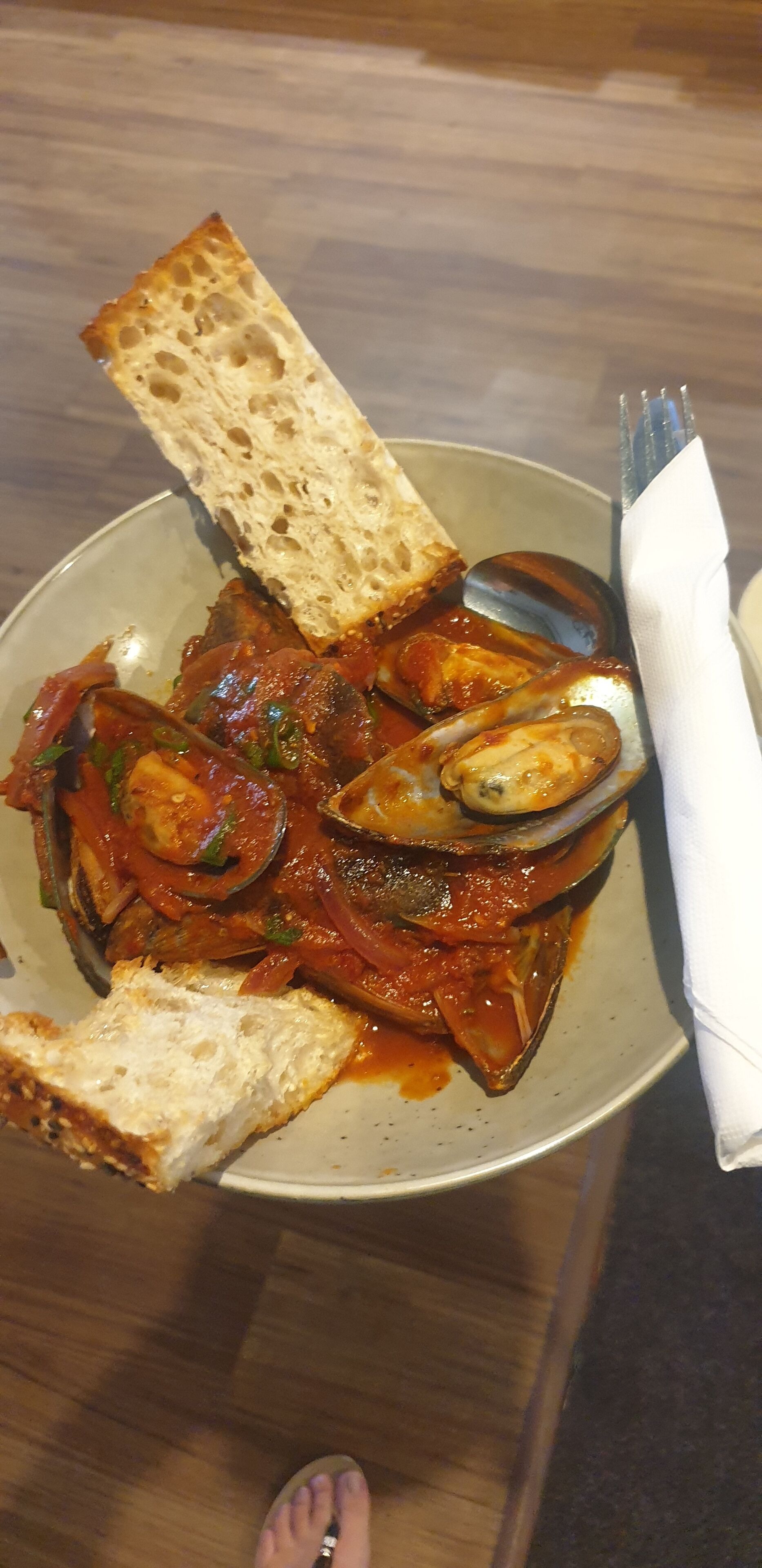 Une assiette de ragoût de fruits de mer, accompagnée de pain et d’une cuillère.