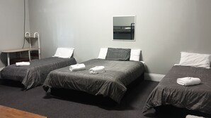 A room with three beds, each with a dark patterned bedspread and white pillows. There is a small table with a chair, a mirror on the wall, and a carpeted floor. - Queens Arms Hotel (Roma)