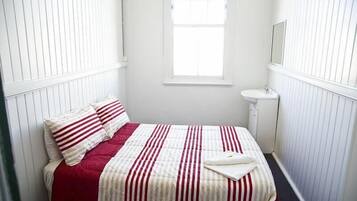 Un dormitorio pequeño con paredes blancas, una cama individual, una mesita de noche y una ventana.
