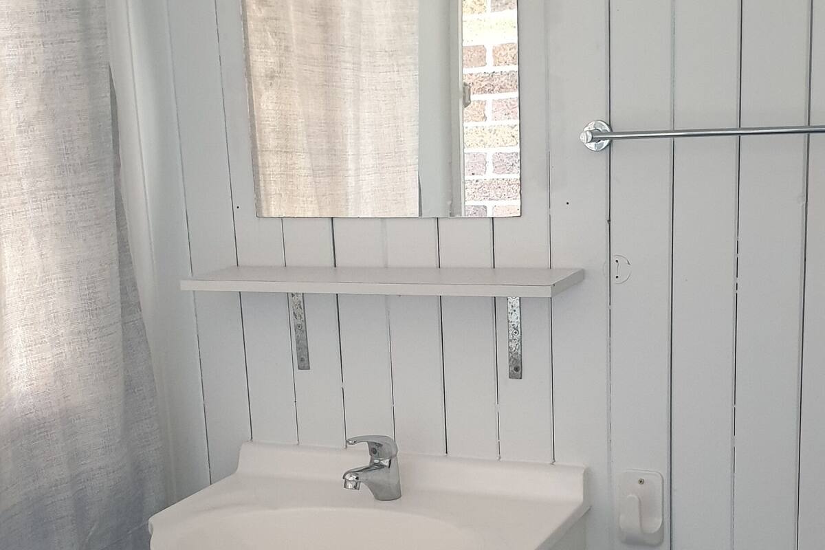 A white bathroom with a sink, mirror, and a towel rack.