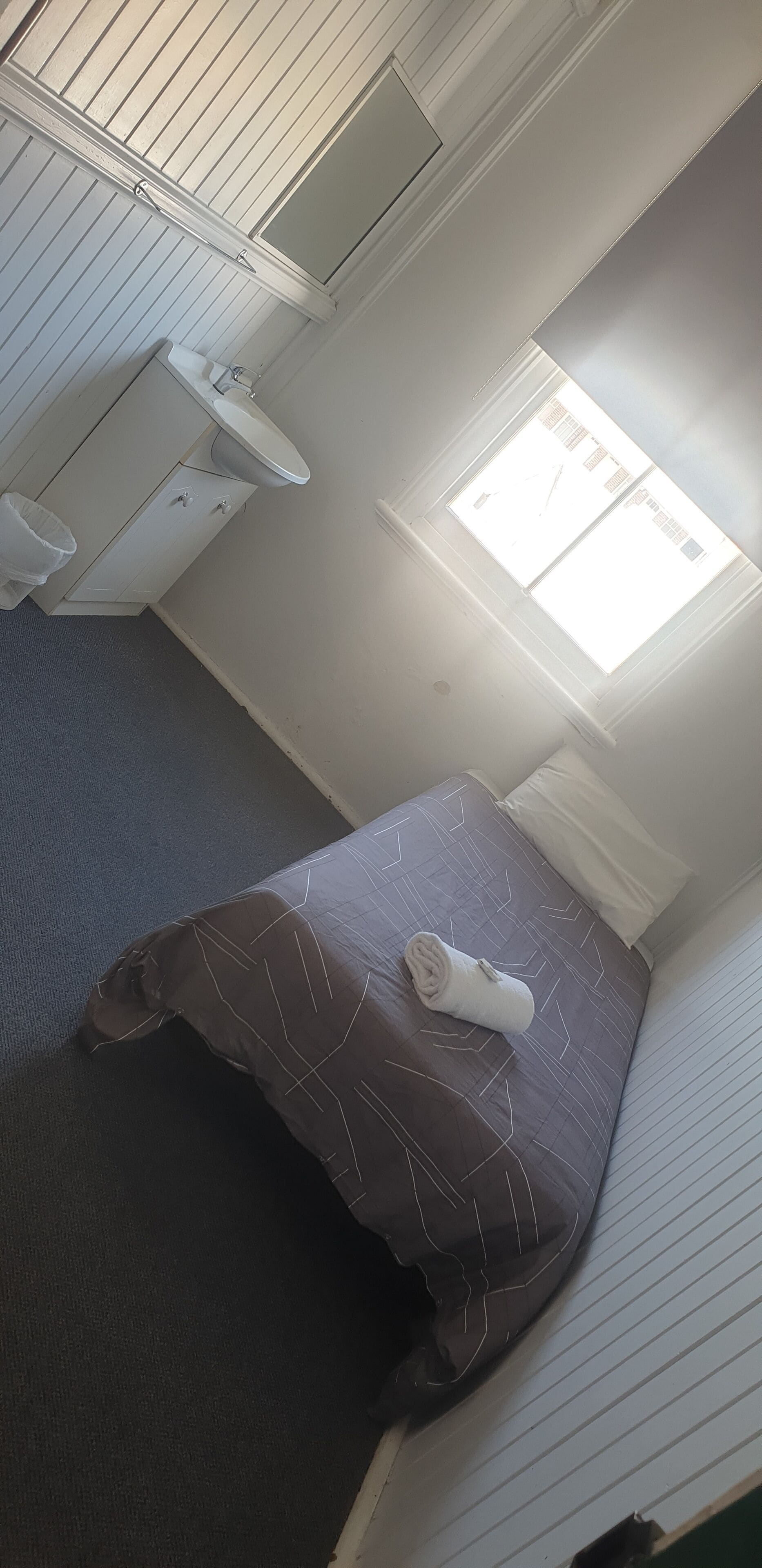 A small, compact room with a single bed, a window, a sink, and a toilet.