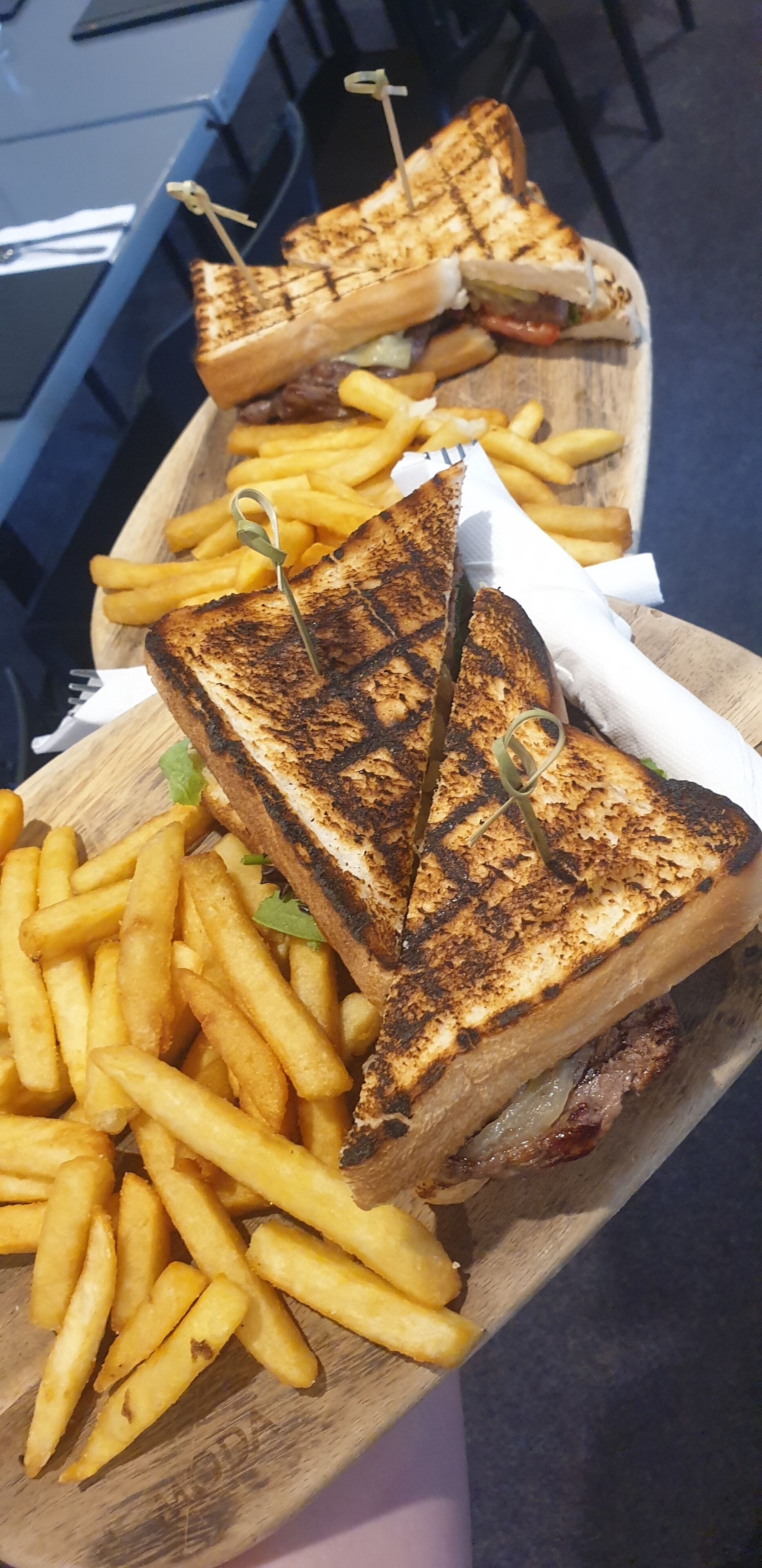 Una bandeja de madera con sándwiches a la parrilla y papas fritas.