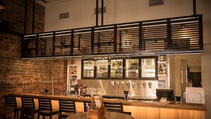 A bar area with a brick wall, wooden bar counter, and multiple seating tables. - Queens Arms Hotel (Roma)