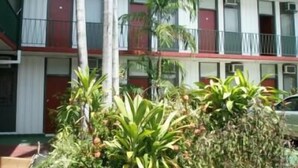 A multi-story motel with a red and white exterior, balconies, and tropical plants in the foreground. - Capricornia Motel (Fannie Bay)