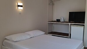 Une chambre avec un lit simple, un petit bureau avec une télévision et une lampe fixée au mur.