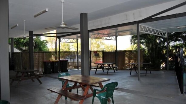 An outdoor patio area with picnic tables and chairs, a ceiling fan, and a view of the surrounding greenery. - Capricornia Motel (Fannie Bay)