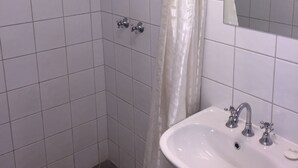 A bathroom with white tiles, a shower with a glass door, a sink with a mirror above it, and a towel rack. - Capricornia Motel (Fannie Bay)