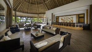 A spacious lounge area with multiple sofas and armchairs, a large artwork on the wall, and a thatched roof ceiling. - Catalonia Yucatan Beach - All Inclusive (Puerto Aventuras)