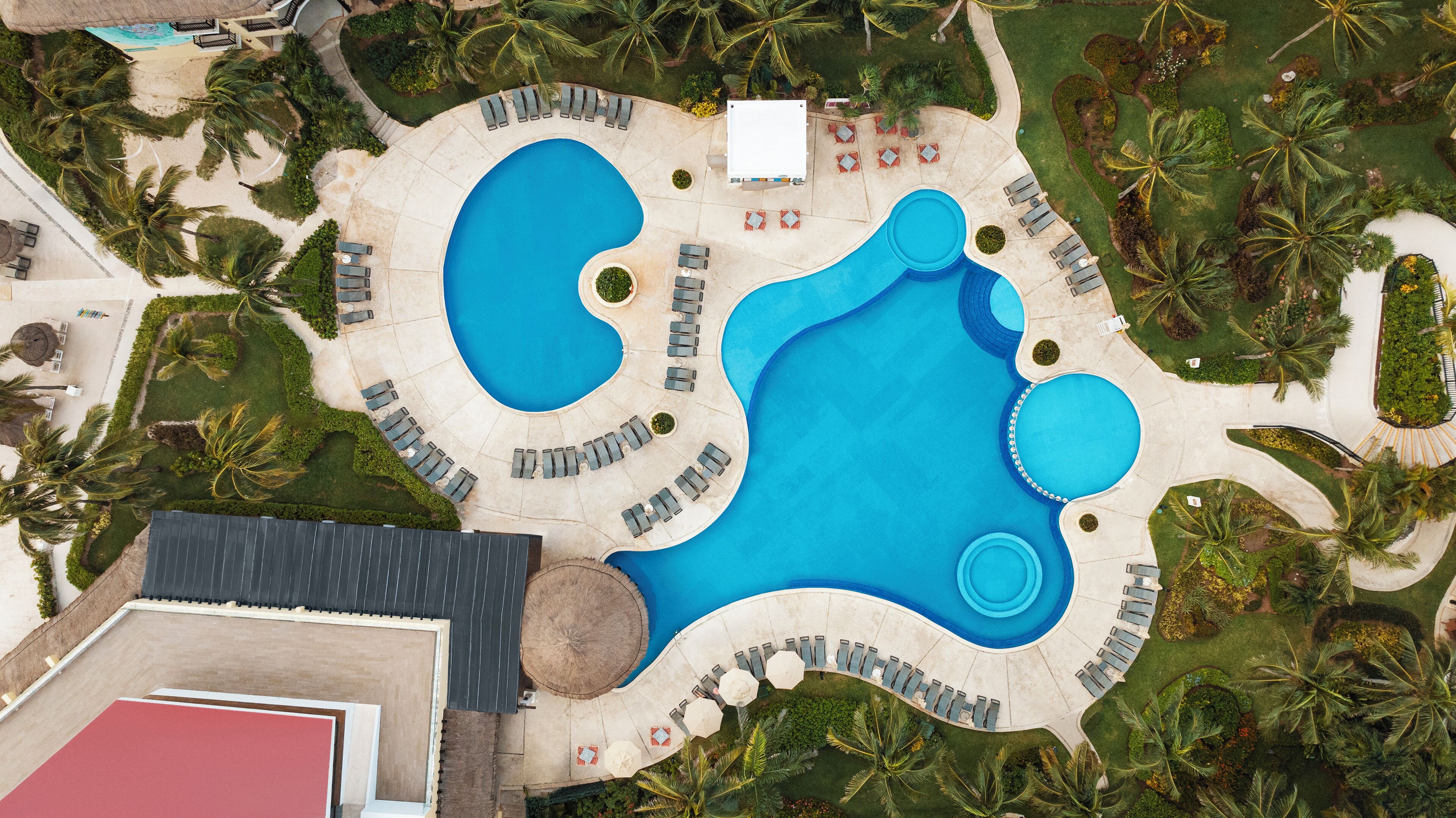 Vista aérea de un resort con varias piscinas, camastros y palmeras.