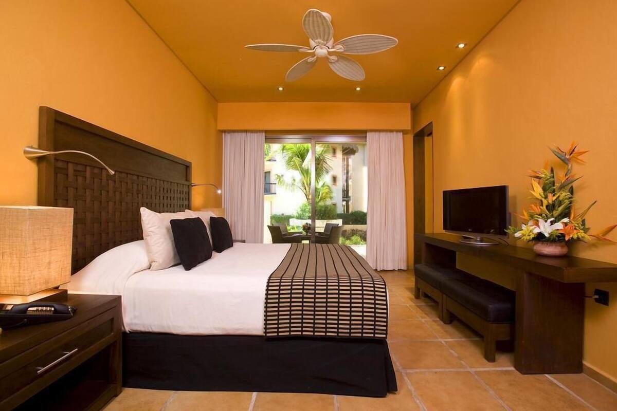 Ein Hotelzimmer mit Bett, Fernseher, Schreibtisch und Deckenventilator.