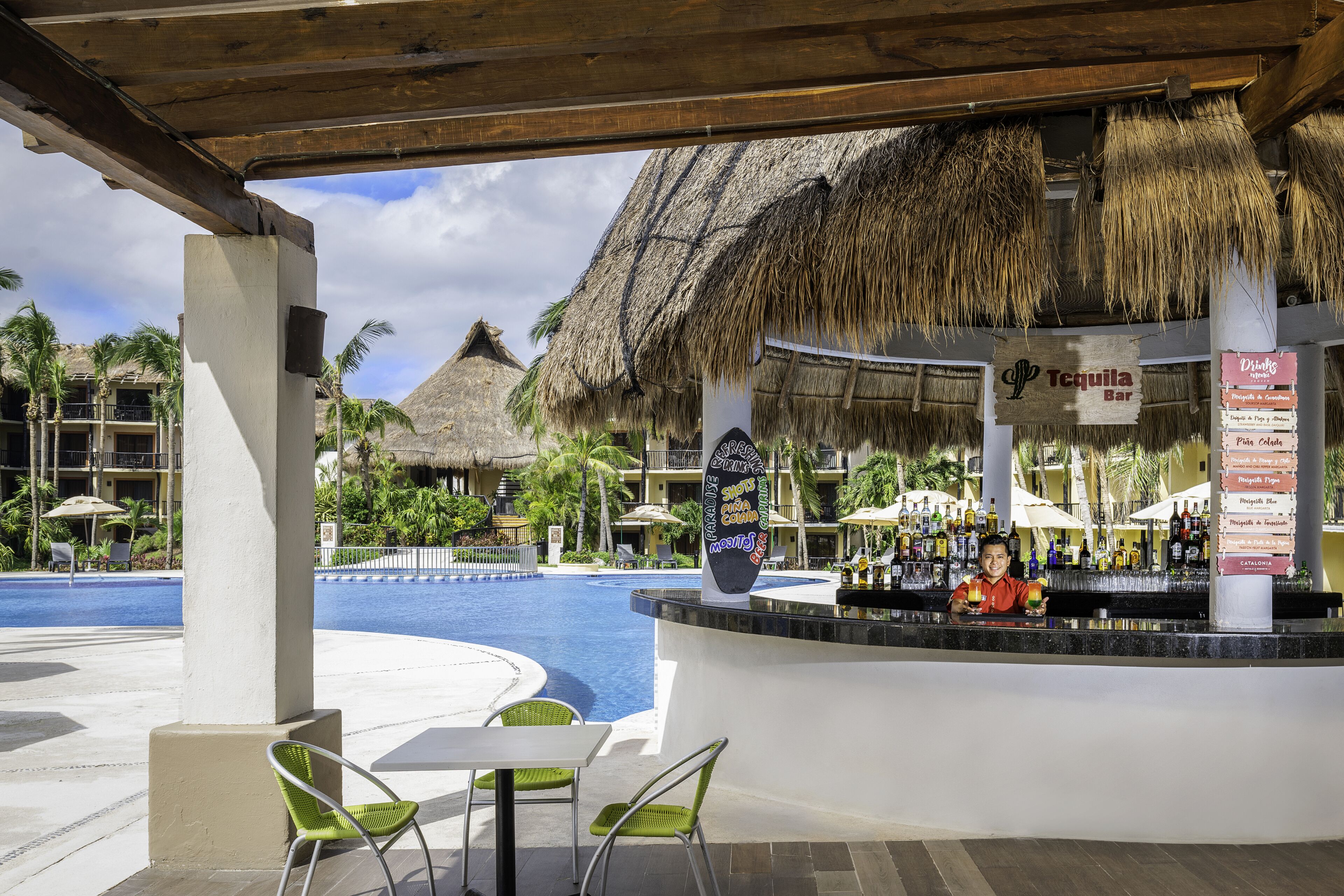 A bar area with a pool view, thatched roof, and a menu board.