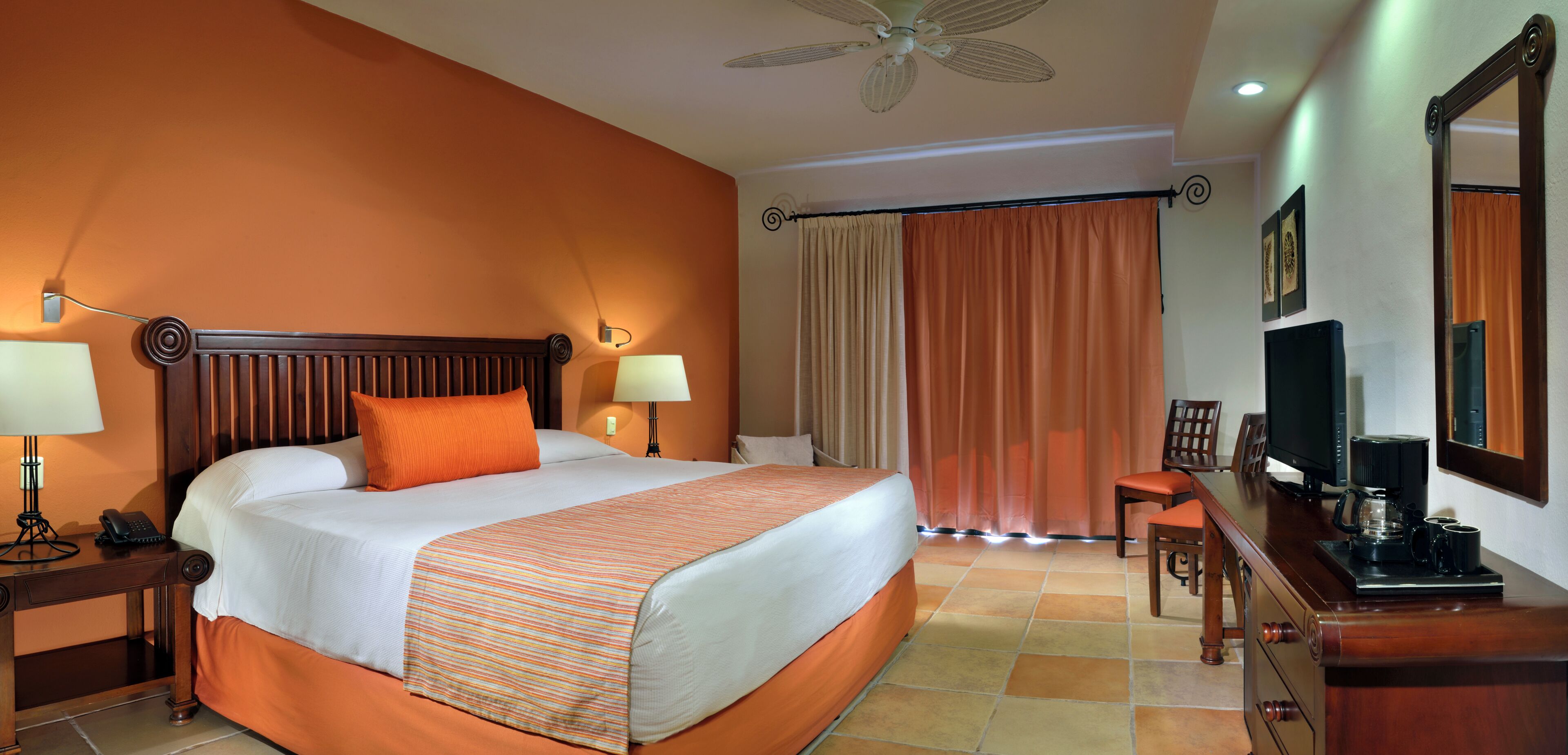 A hotel room with a bed, bedside lamps, a desk with a television, and a ceiling fan.