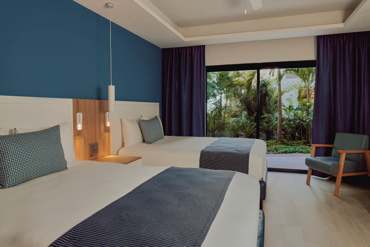 Ein modernes Hotelzimmer mit zwei Betten, einem Holzkopfende, einem großen Fenster mit Blick auf Grünflächen und einem Sessel.