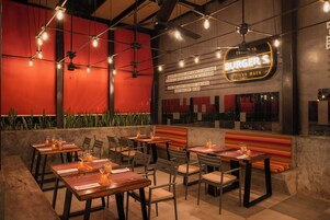 Un área de comedor al aire libre con mesas y sillas, un letrero de neón para Burger's y una pared roja.