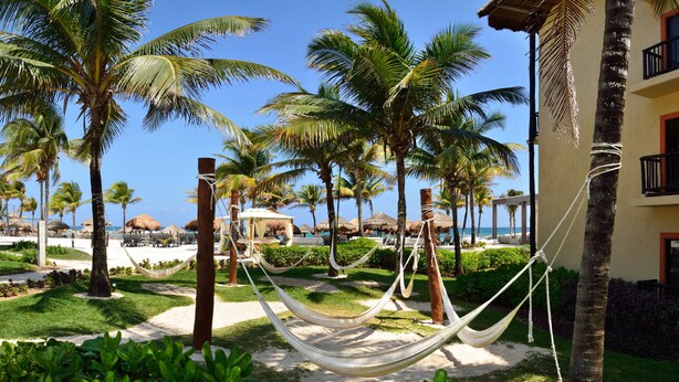 A resort with palm trees, a hammock, and a pool area. - Catalonia Yucatan Beach - All Inclusive (Puerto Aventuras)