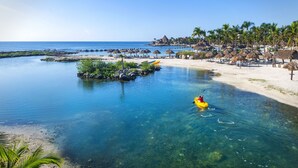 A beach with clear water, a kayak, and thatched-roof structures. - Catalonia Yucatan Beach - All Inclusive (Puerto Aventuras)