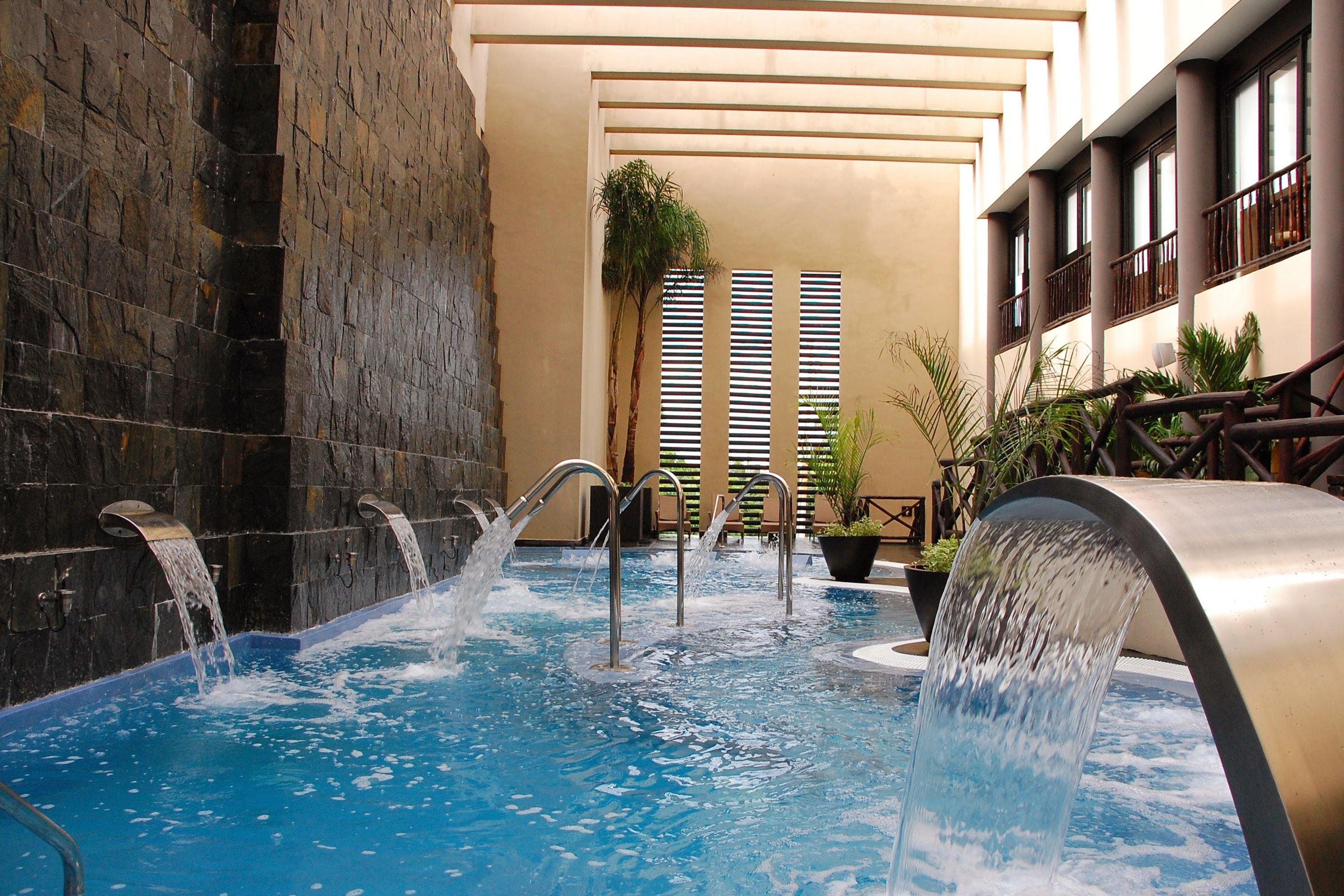 An indoor swimming pool with multiple water jets, surrounded by stone walls and potted plants.