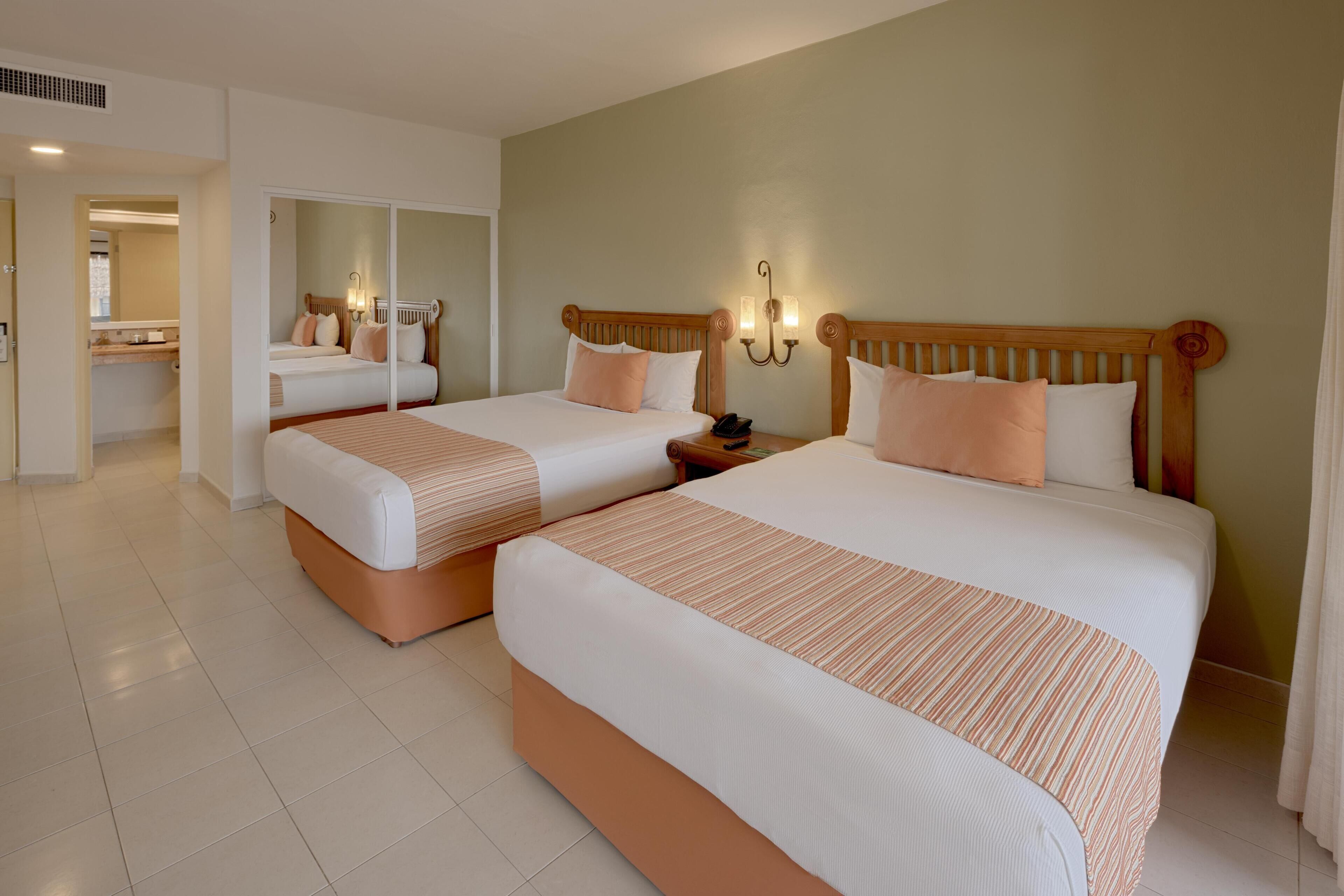 Habitación de hotel con dos camas, un espejo, una mesita de noche y una lámpara de pared.
