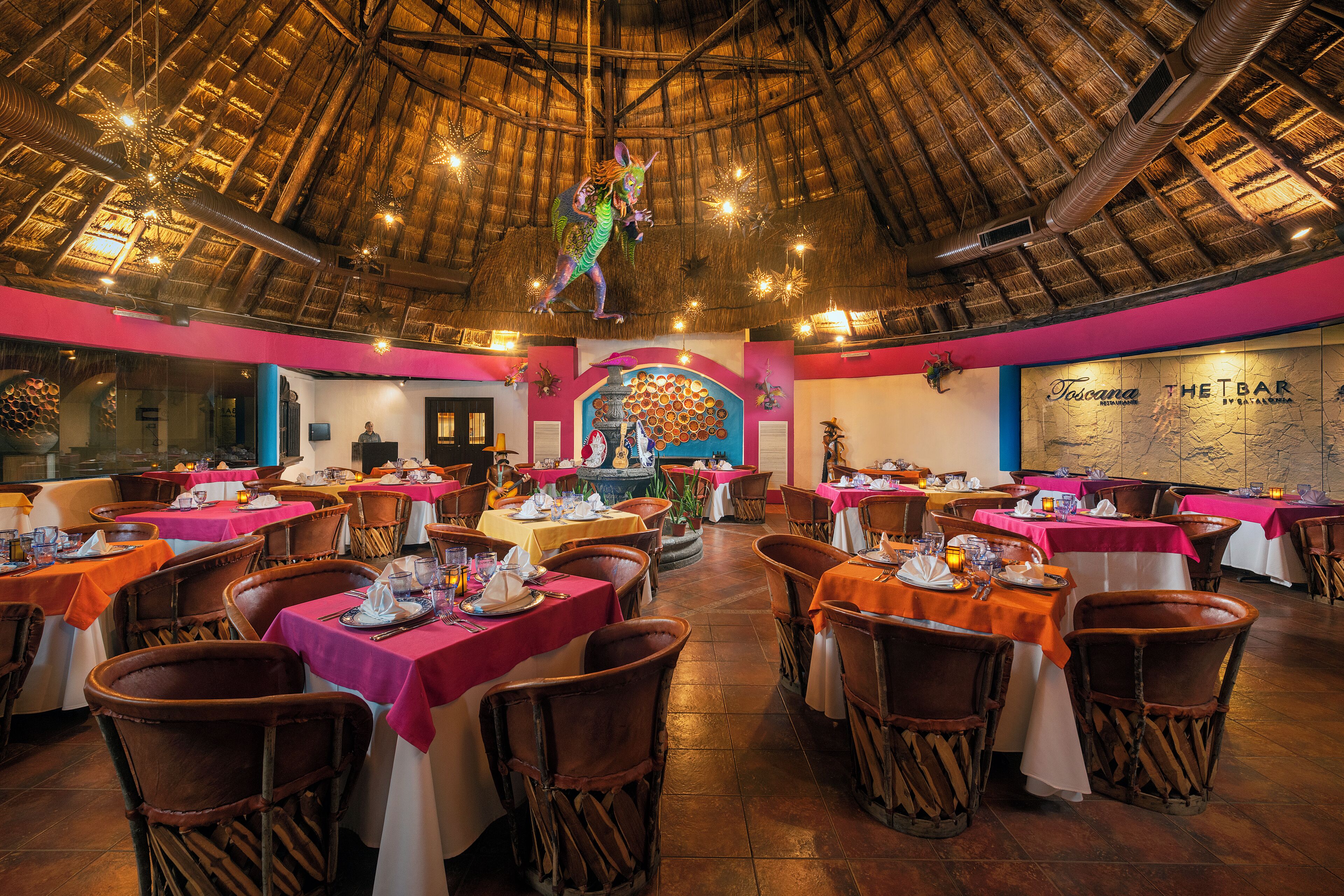 Un restaurant avec des tables dressées pour le service, un plafond en chaume et une fresque murale.