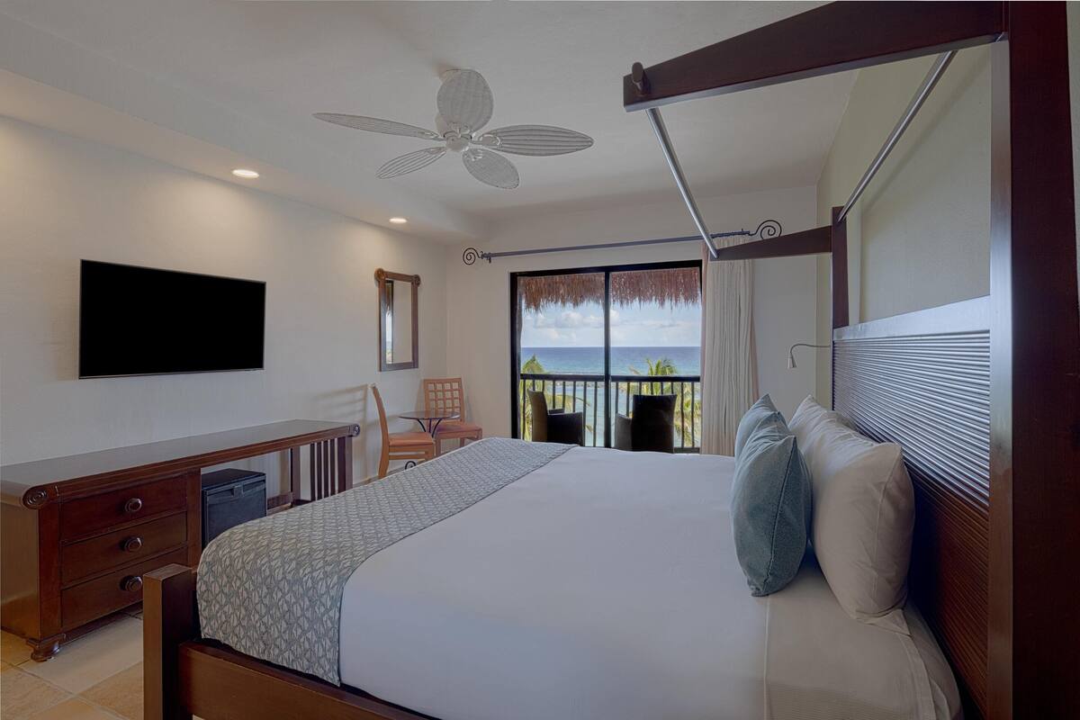 Ein Hotelzimmer mit Bett, Schreibtisch, Stuhl, Fernseher und einem Balkon mit Meerblick.