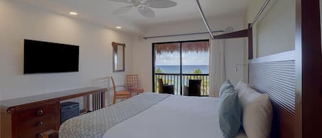 Habitación de hotel con cama, escritorio, silla, televisor y balcón con vista al océano.