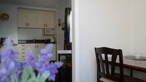 A compact kitchen with white cabinets, a microwave, and a dining area with a wooden chair and table. - Admirals Lodge Picton (Picton)
