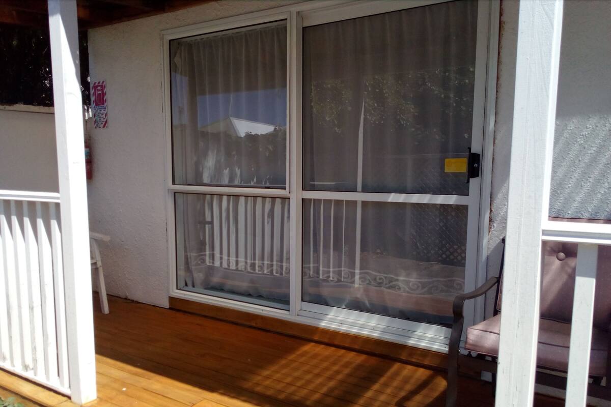 A screened porch with a white railing, a bench, and a view of a house through the window.